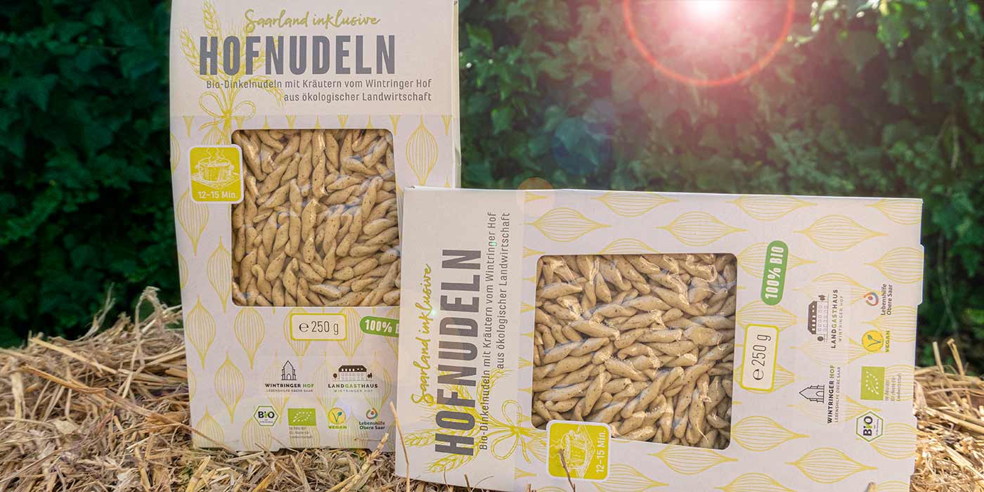 Zwei Packungen der Saarland inklusive-Dinkel-Hofnudeln auf einem Strohballen