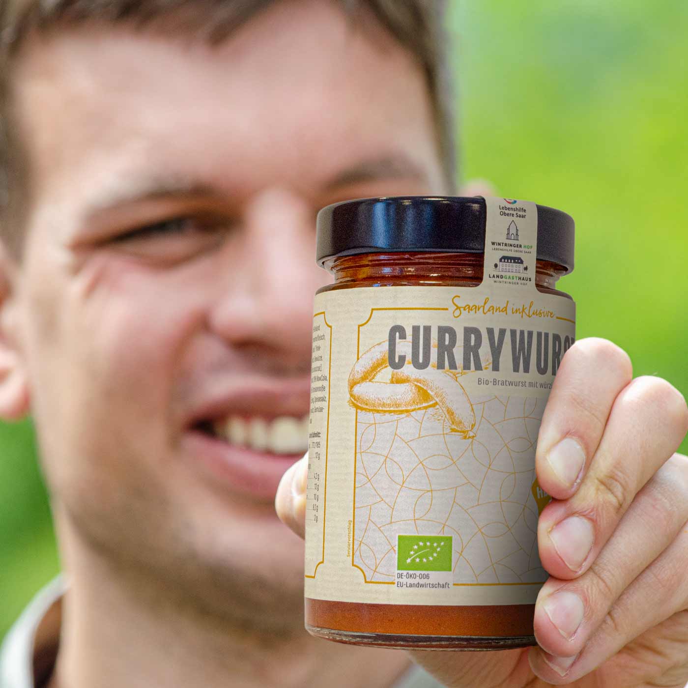 Ein Inklusionsmitarbeiter hält ein Glas Saarland inklusive-Currywurst in die Kamera